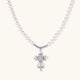 White pearl necklace with ornate silver cross pendant featuring zirconia crystals on cream background.