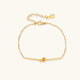 Delicate gold chain bracelet with minimalist bar and centered knot detail on cream background